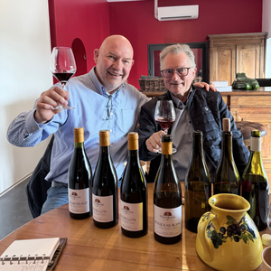 Two men sitting at a table with wine bottles and glasses, one holding a glass of gamay wine.